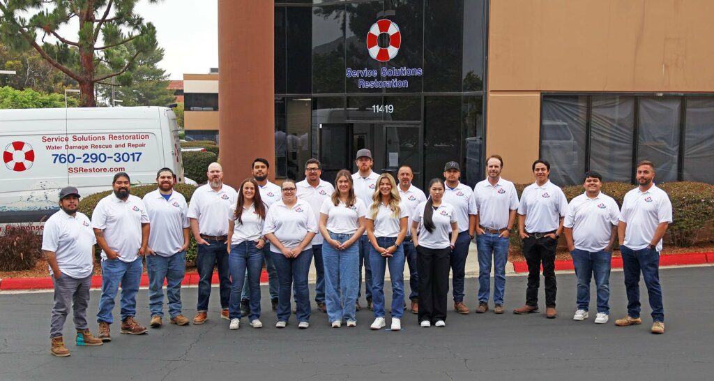A group of 17 people in uniform posing in front of a building and a company vehicle marked "Service Solutions Restoration."